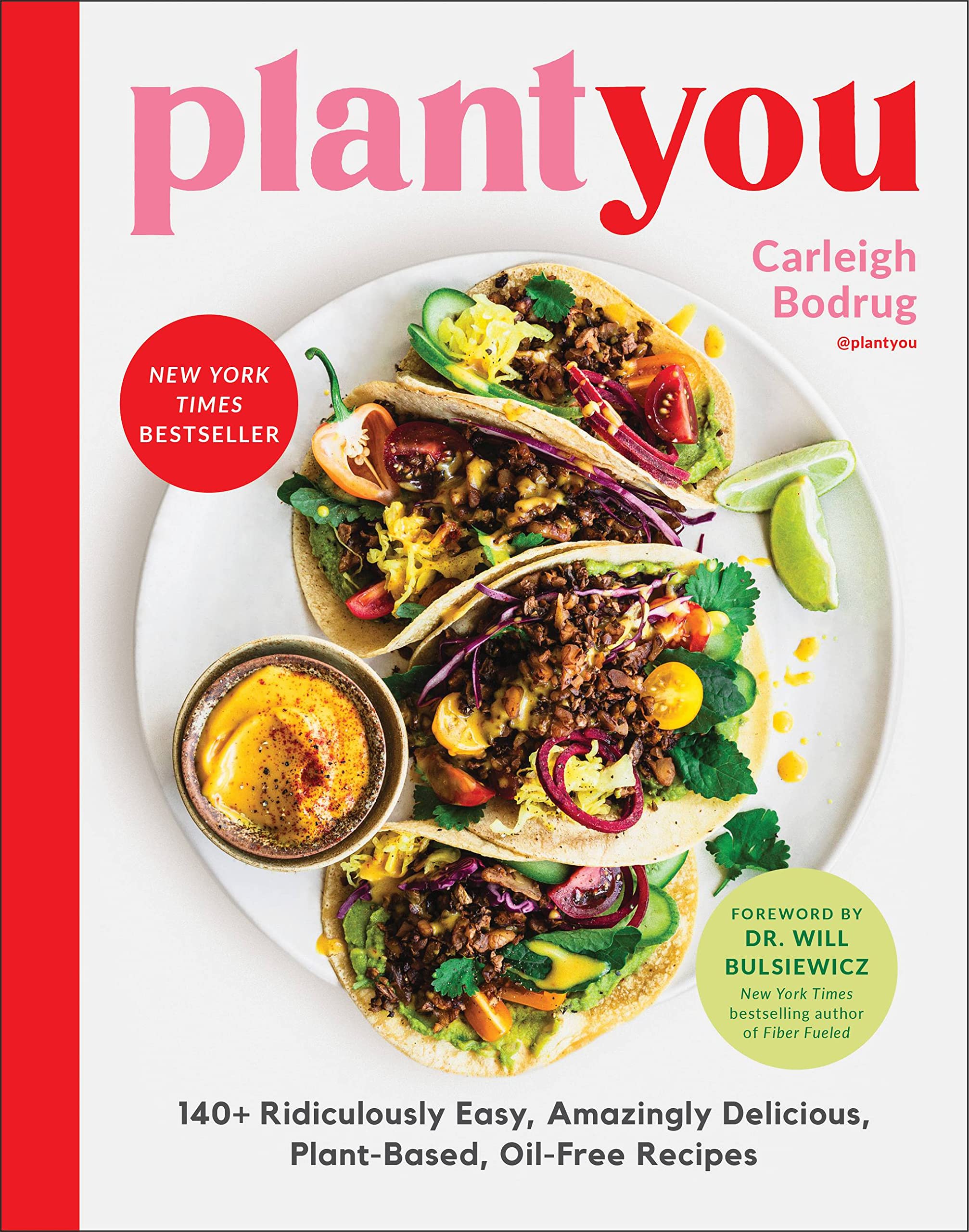 Hardback book "PlantYou" by Carleigh Bodrug and Dr. Will Bulsiewicz on a wooden table with a plant in the background.
