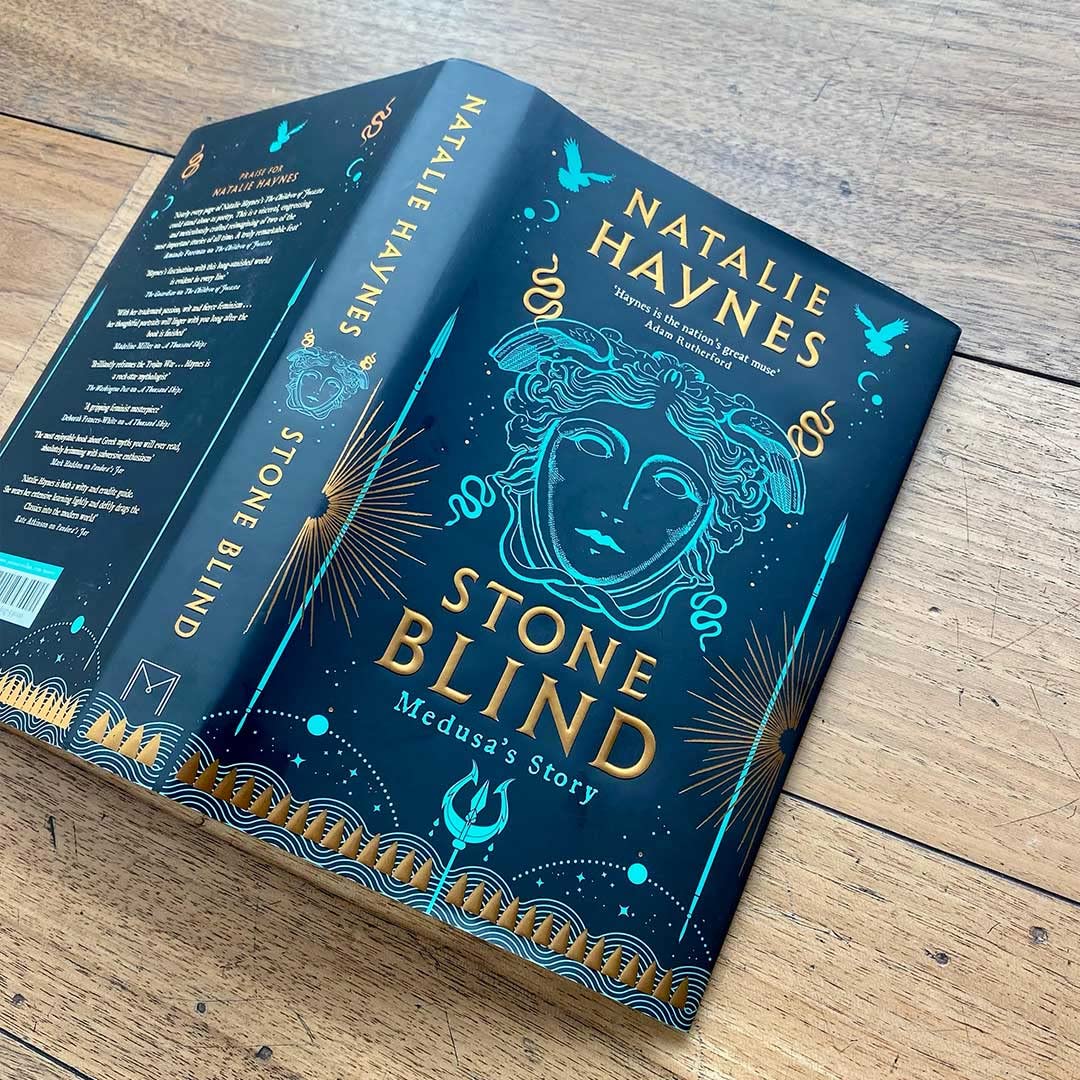 Hardback edition of "Stone Blind" by Natalie Haynes displayed on a mantel, featuring a colorful cover design.